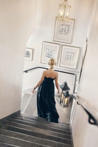 Kvinna i elegant klänning går nerför trappa med tända ljuslyktor på Villa Aske inför julfest nära Stockholm.